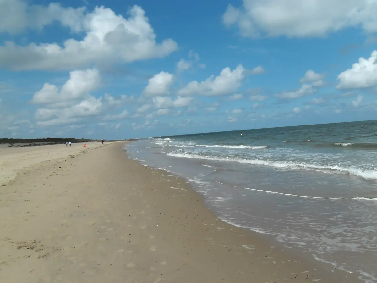 Breiter Sandstrand bei Renesse mit kleinen Wellen und Dünen im Hintergrund.